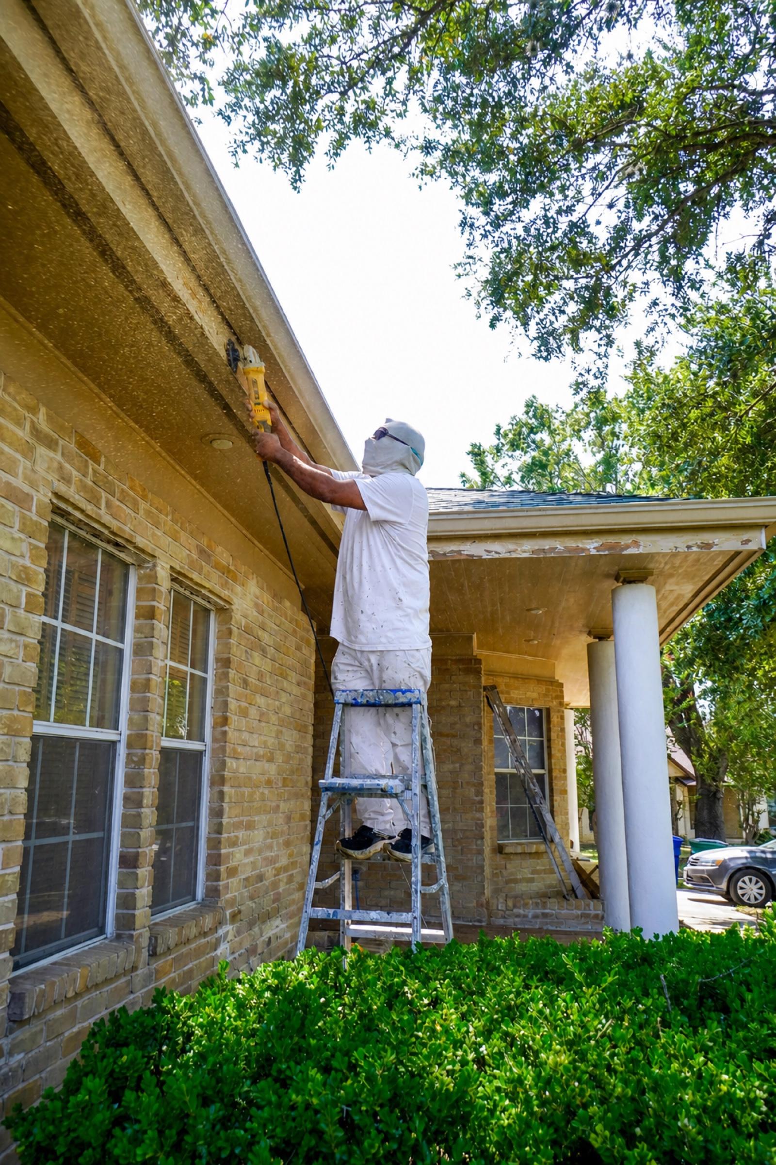 A.C.L. Painting worker in painter’s whites sanding an exterior eave