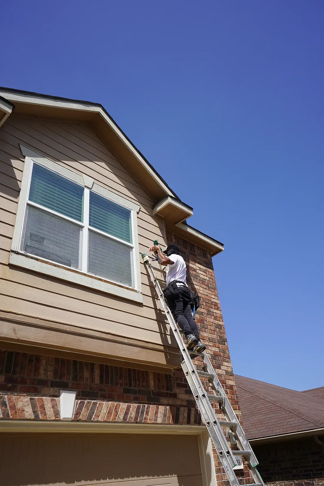 A.C.L. Painting worker on a ladder painting the upper garage gable